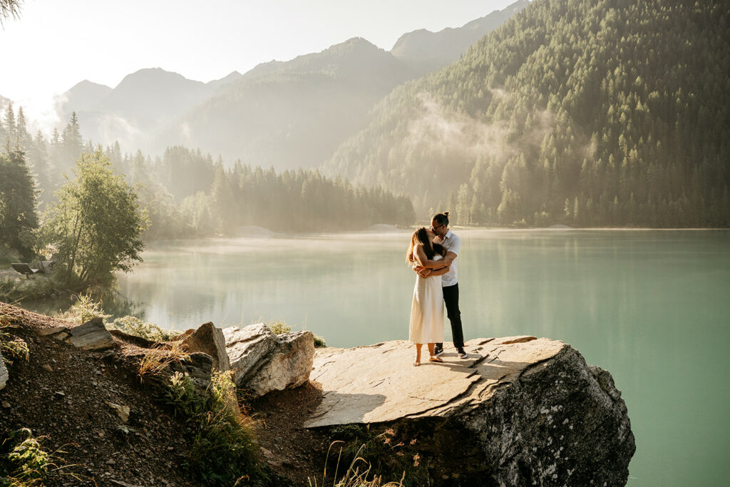 Couple embraces on cliff by serene mountain lake.