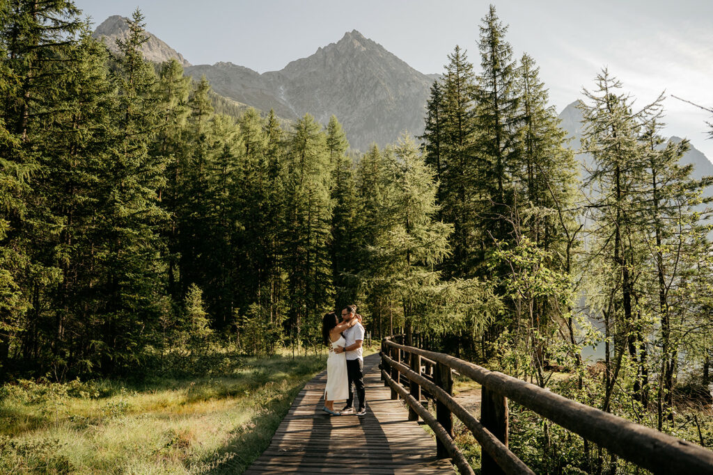 Couple embraces on forest boardwalk with mountain view.