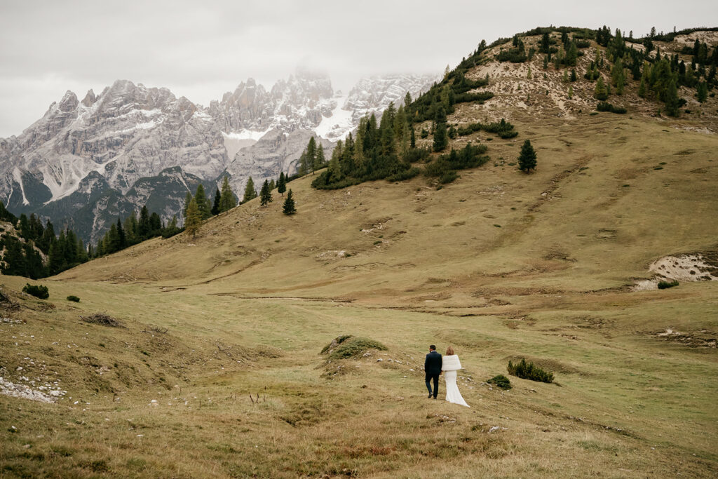Couple walking on mountain landscape with cloudy sky.
