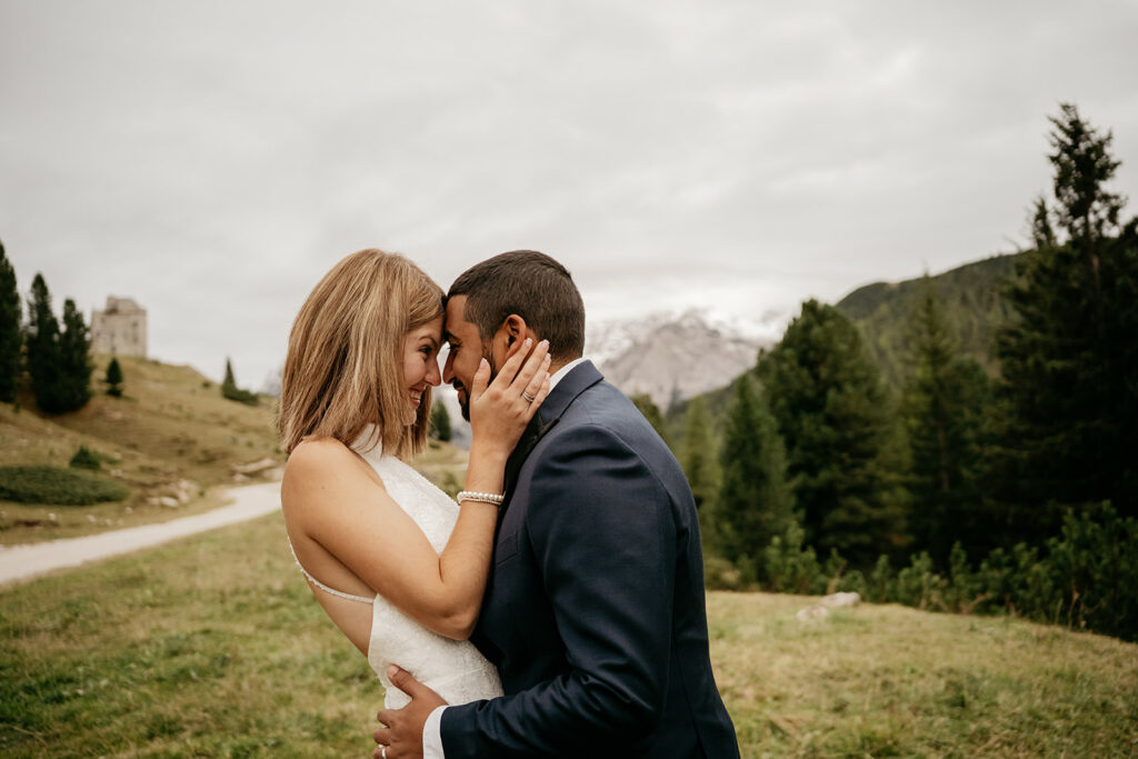 Couple embraces outdoors near mountains and trees.