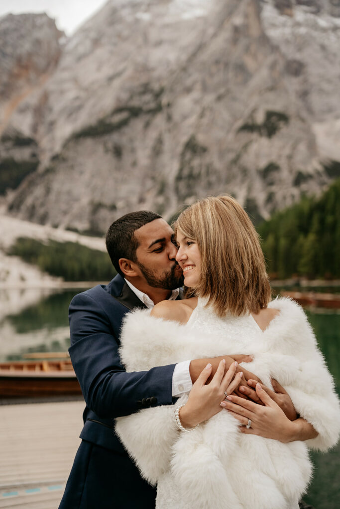 Couple embracing near mountain lake backdrop.