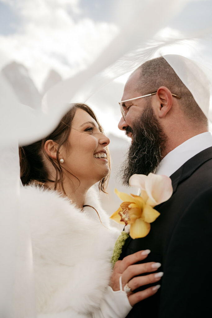 Smiling couple in wedding attire embracing outdoors.