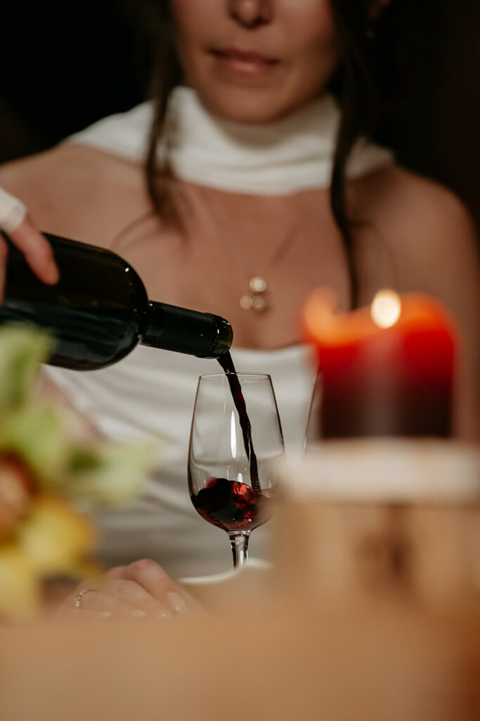 Red wine poured into glass, woman blurred, candlelit