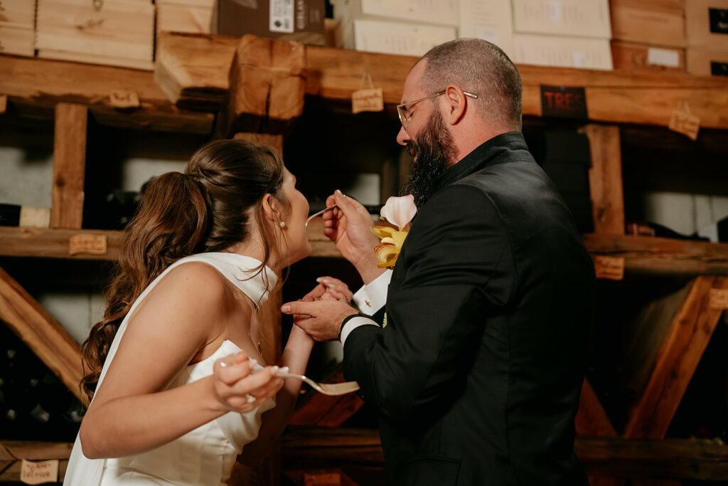 Couple playfully feeding each other cake at wedding.
