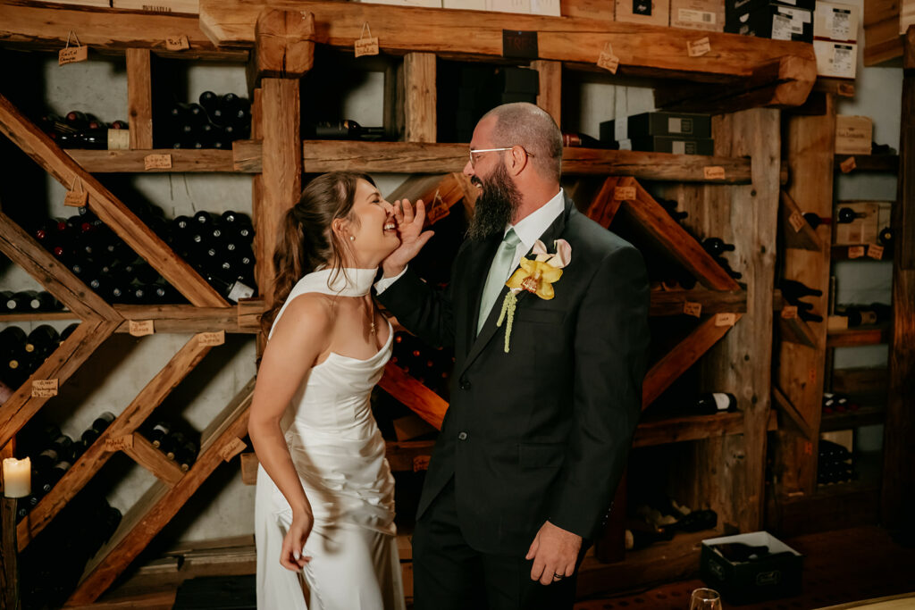 Laughing bride and groom in wine cellar moment.