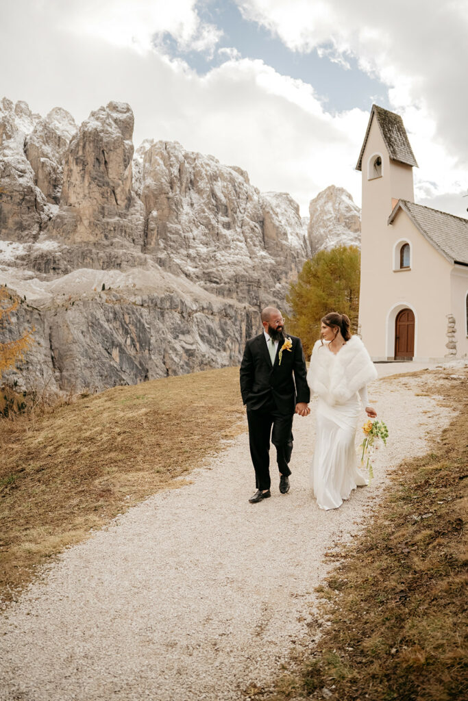 Couple walking in mountain wedding setting with chapel.
