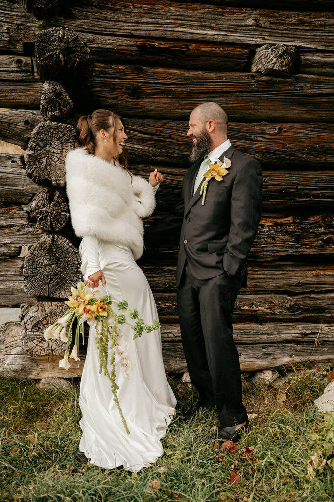 Bride and groom smiling by rustic log wall.