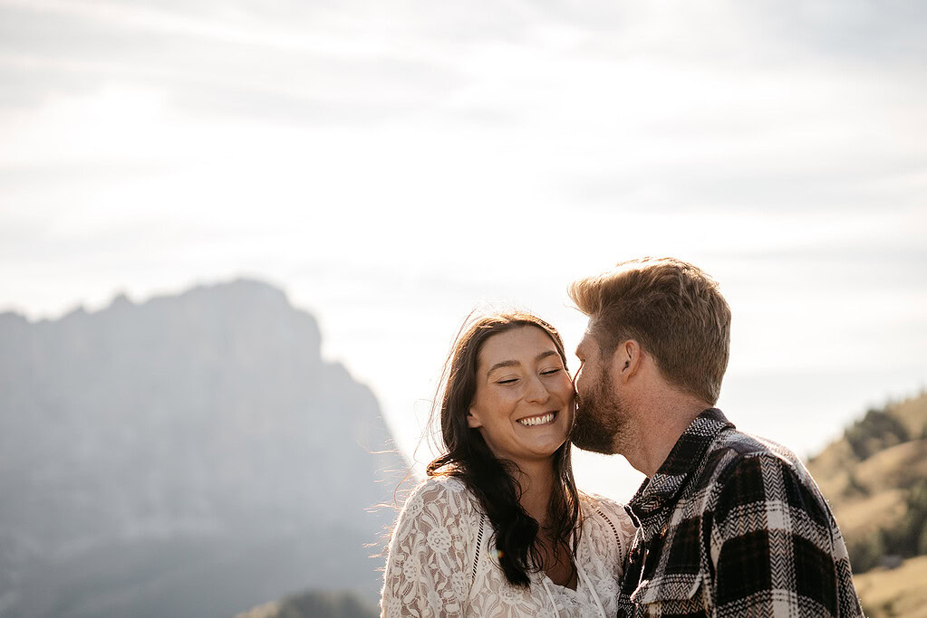 Couple smiling in mountain landscape at sunset.