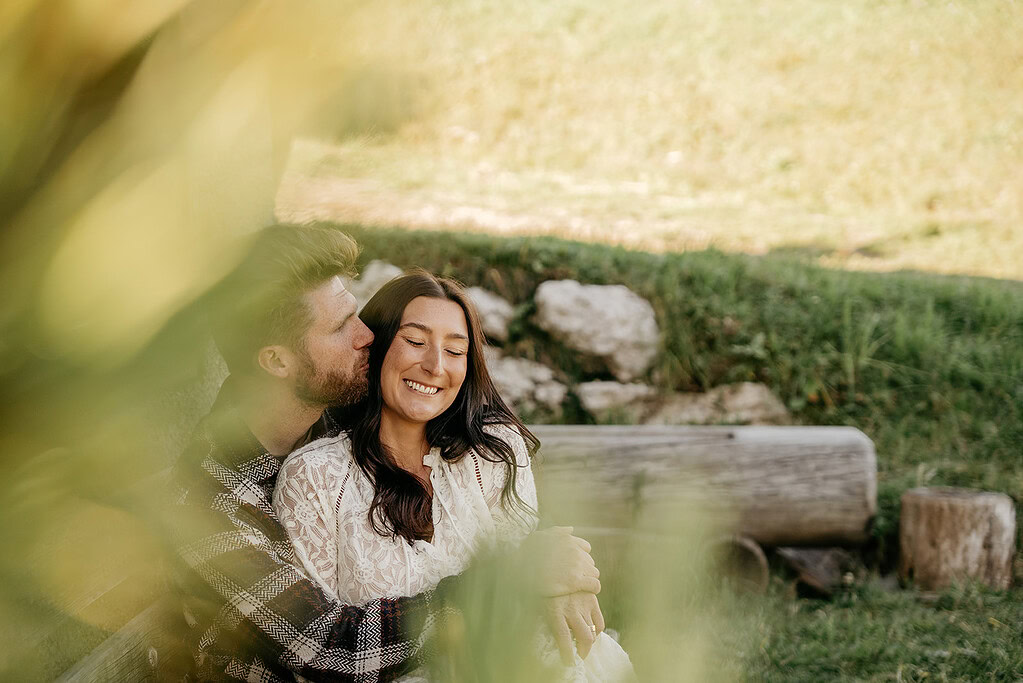 Smiling couple embraces outdoors on grassy hillside.