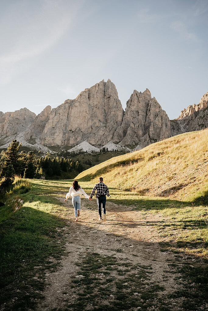 Couple running towards mountains on a sunny trail.