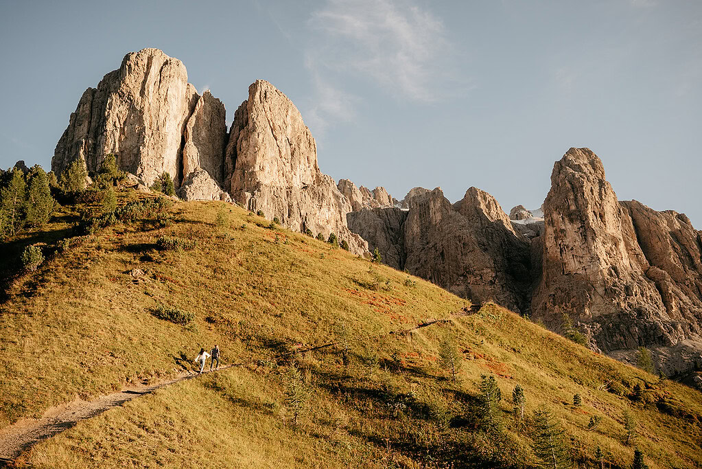 Hikers on path towards rocky mountain peaks at sunrise.