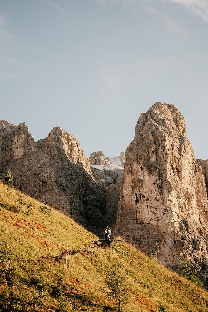 Hikers on grassy slope with towering cliffs behind.