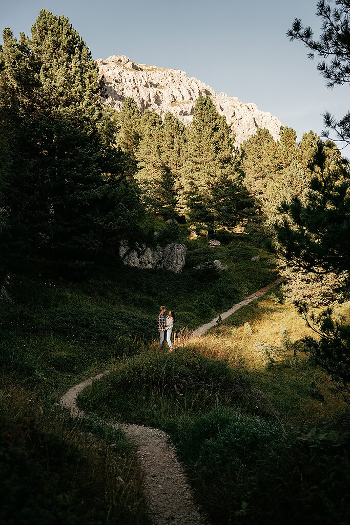 Couple standing on forest path in mountain clearing.