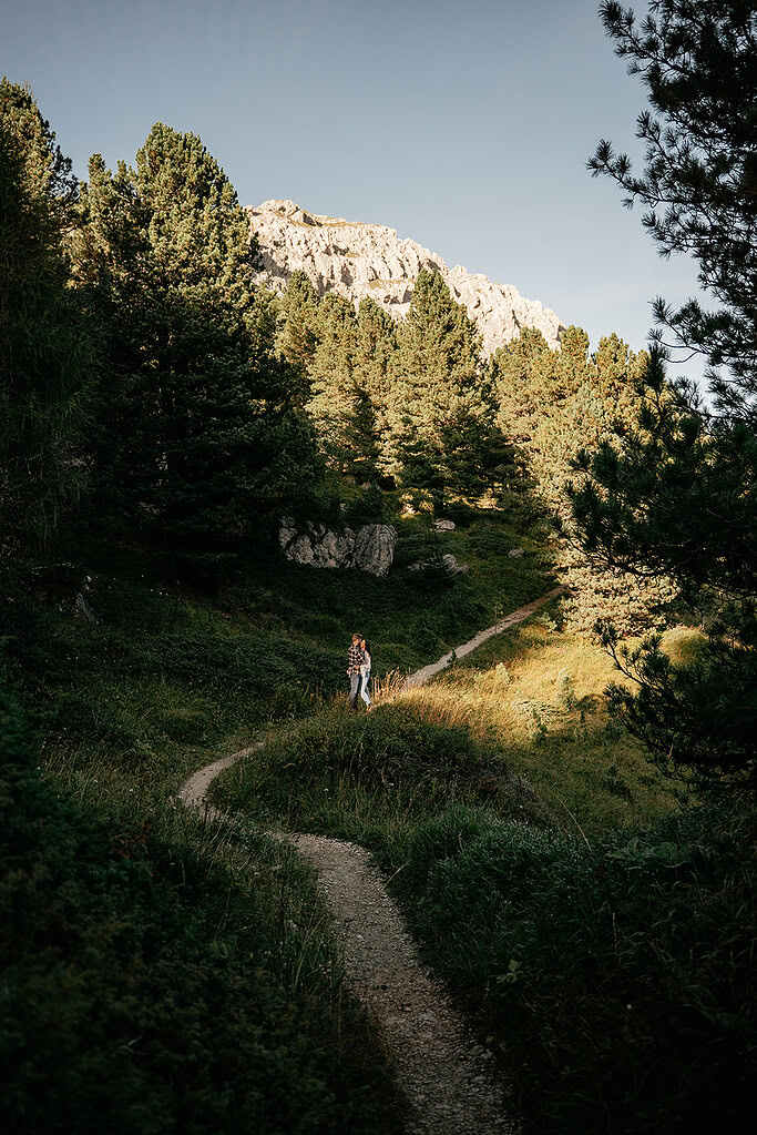 Couple hiking on forest trail, mountain background.