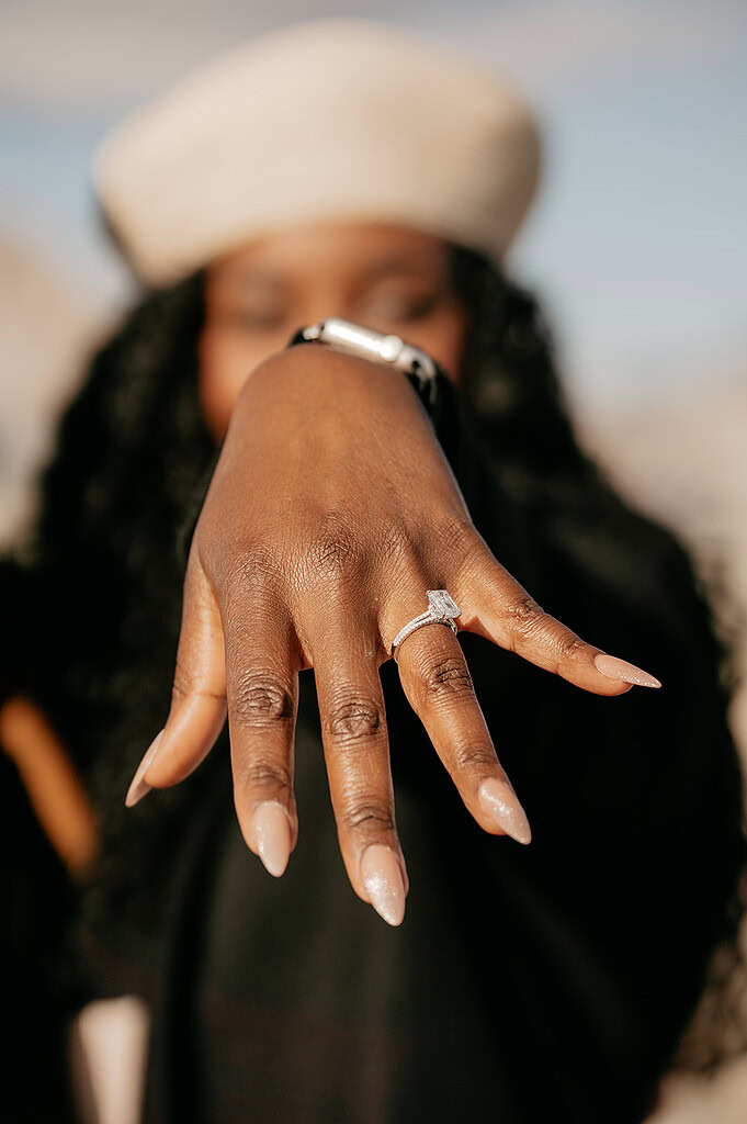 Woman displaying diamond engagement ring on finger.