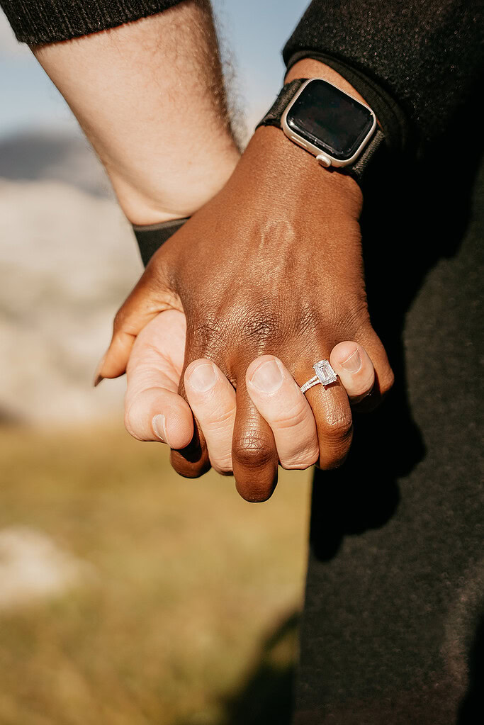 Couple holding hands, engagement ring visible.