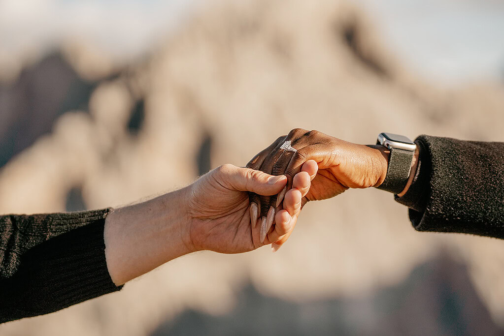 Two hands holding, one with an engagement ring.