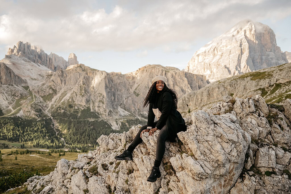 Smiling woman sitting on mountain rocks in sunshine.