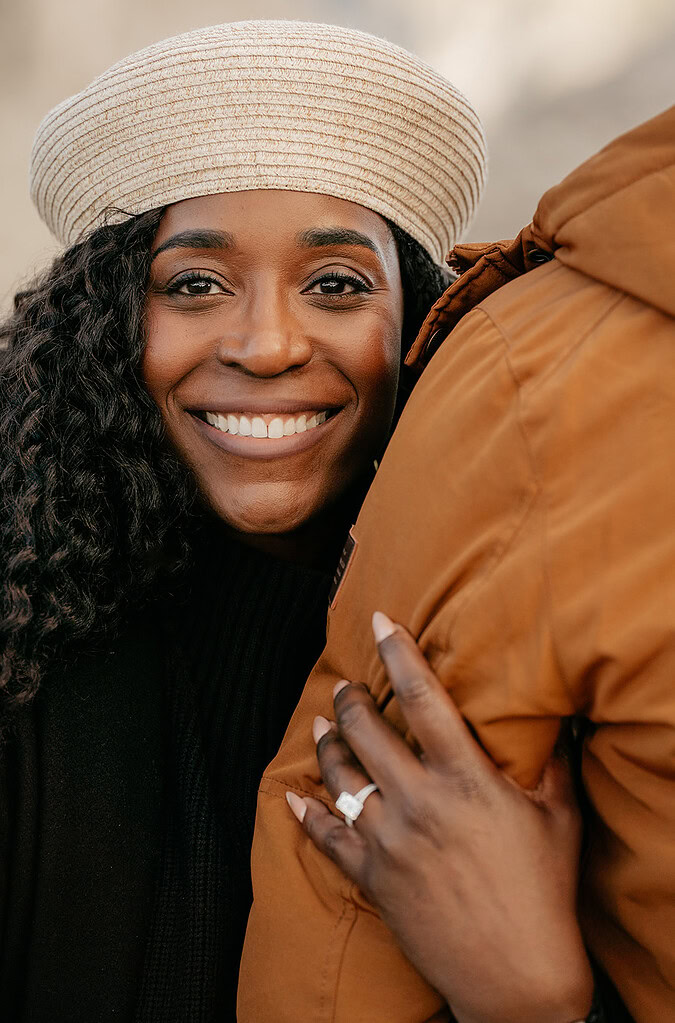 Smiling woman in beret hugs partner's arm.