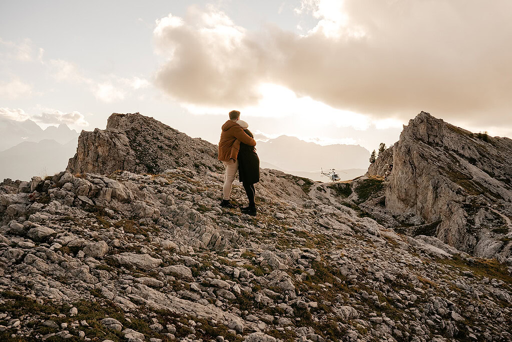 Couple embraces on rocky mountain at sunset.