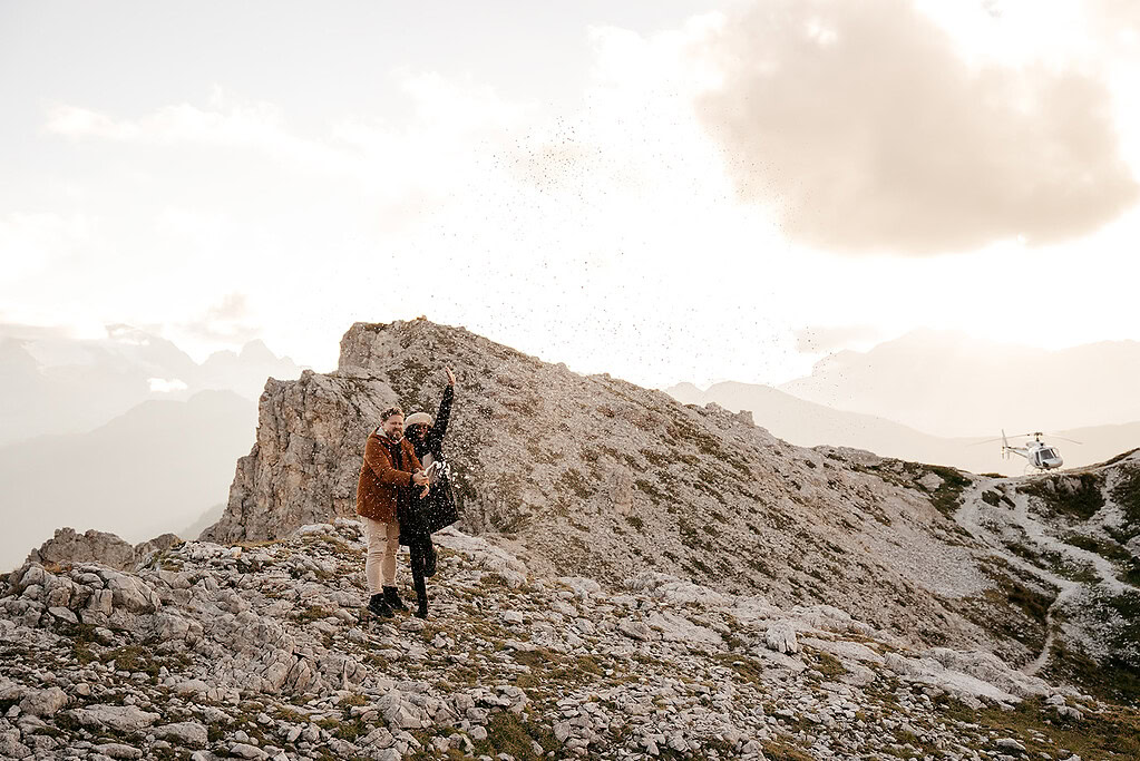 Couple celebrates on rocky mountain with champagne.