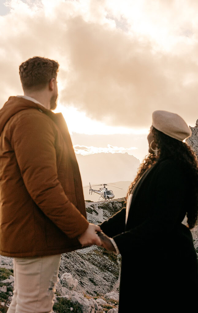 Couple holding hands, helicopter landing on mountain