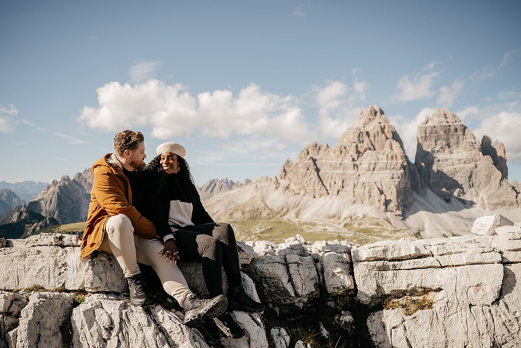 Couple sitting on rock in mountain landscape.
