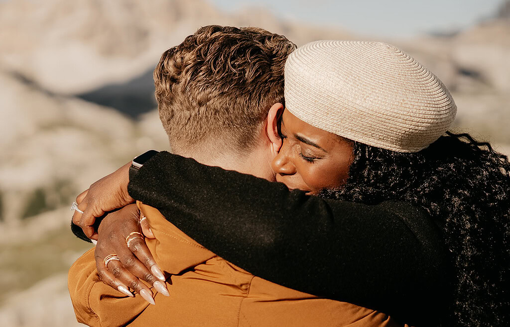 Couple embracing outdoors with mountains backdrop.