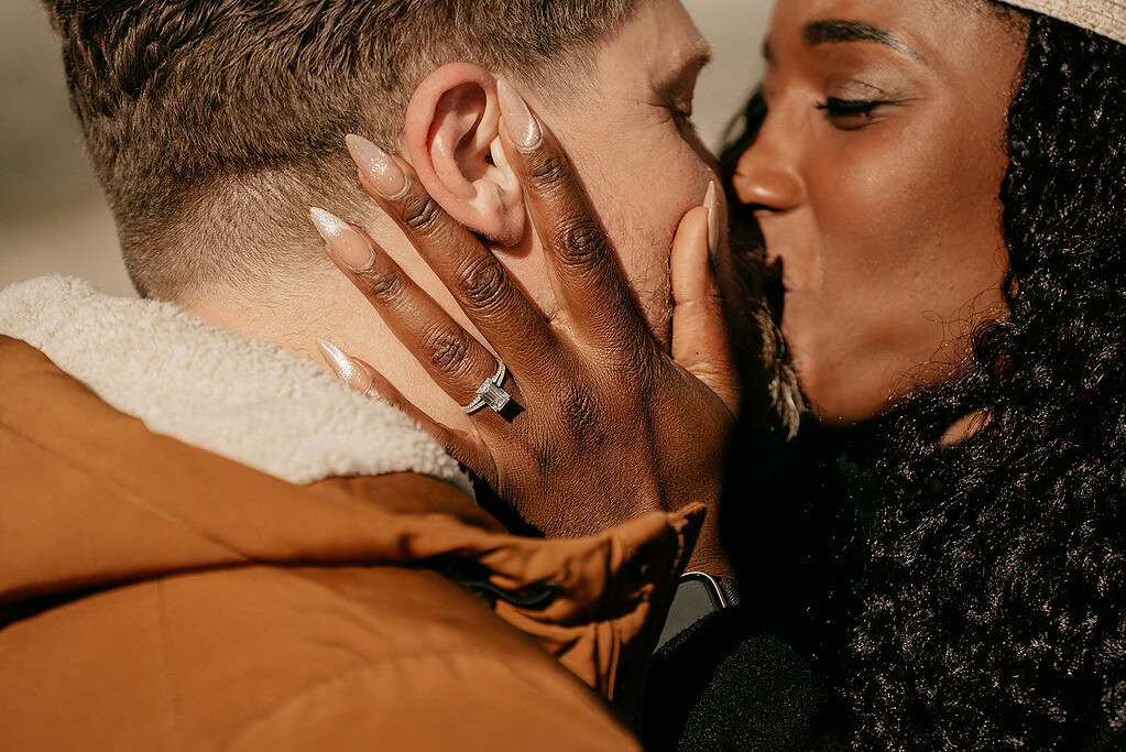 Couple kissing, engagement ring visible on woman's hand.