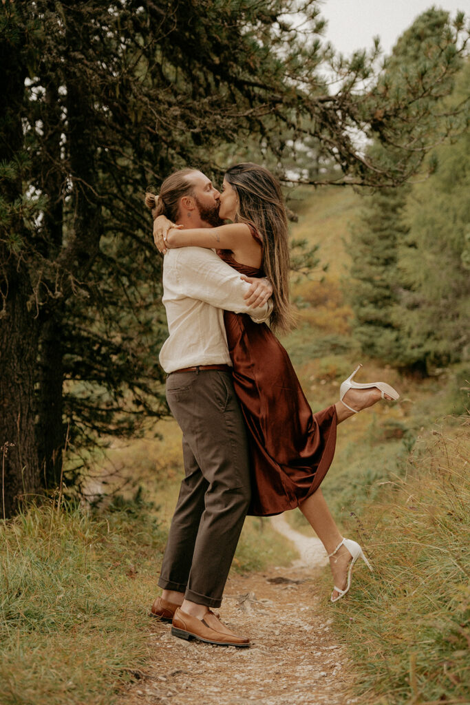 Couple embracing in nature, surrounded by trees.
