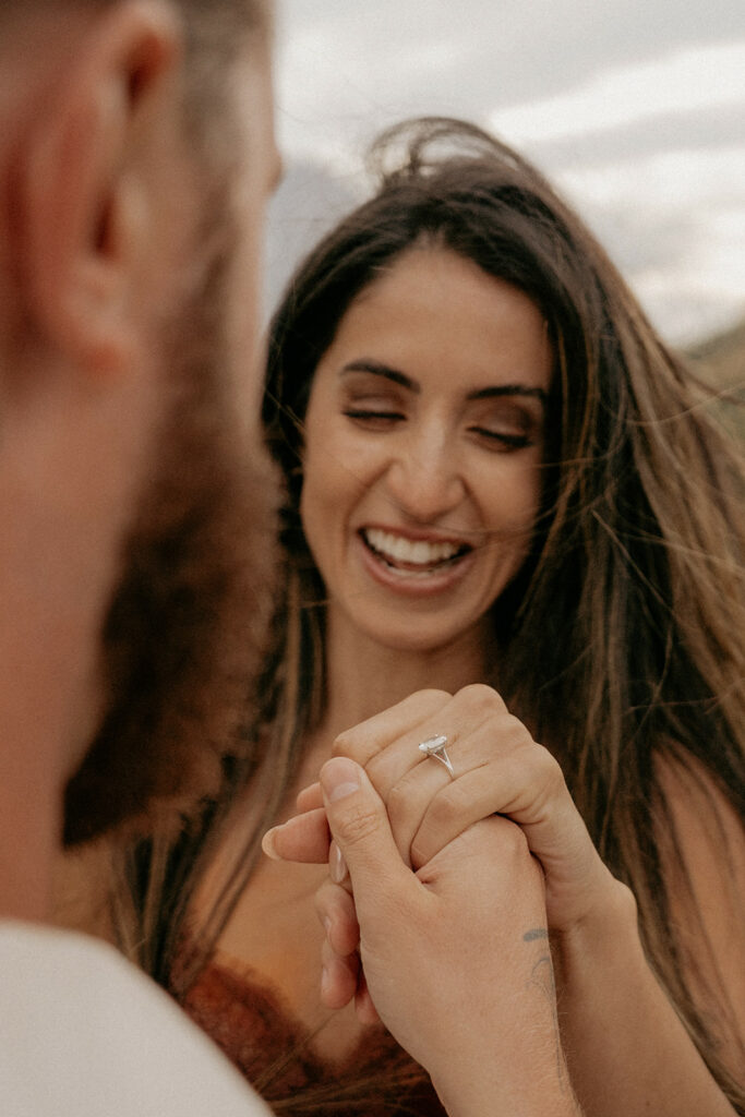 Engaged couple holding hands, woman smiling with ring.