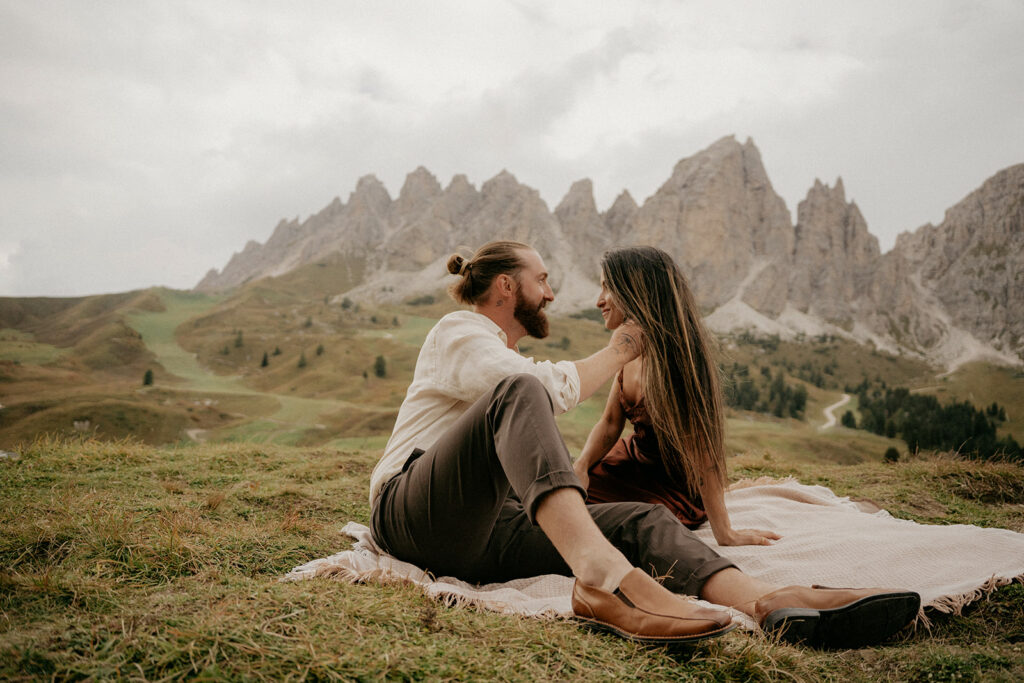 Couple sitting on blanket in mountain landscape.