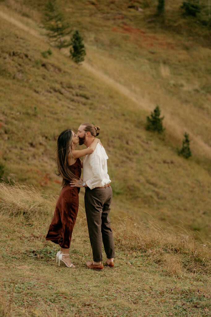Couple kissing on a grassy hill.