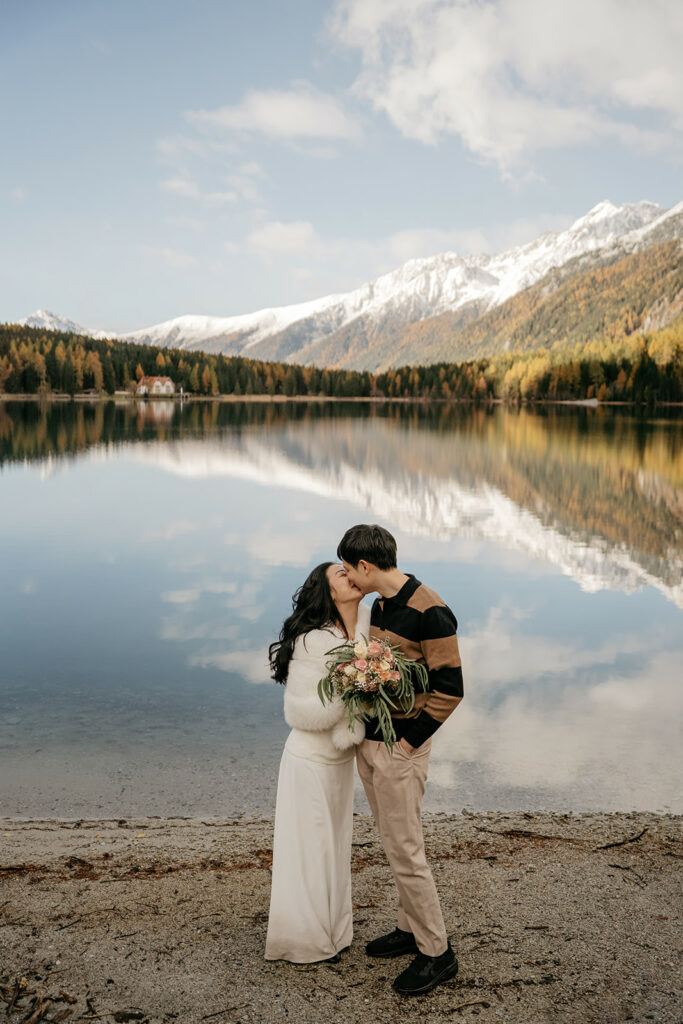Couple kissing by lake with mountain backdrop