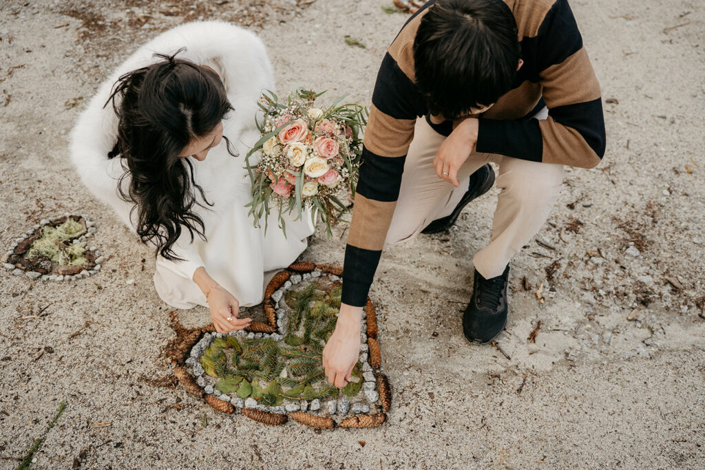 Couple arranging heart-shaped natural art on sand