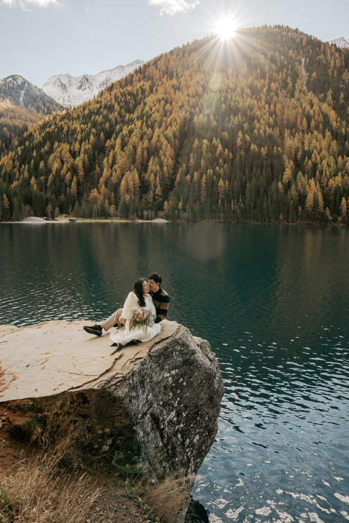 Couple sitting on lakeside rock with mountain view.