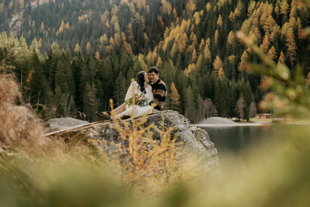 Couple sits on rock by forest and lake