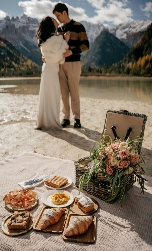 Couple kissing near picnic setup and scenic mountains.
