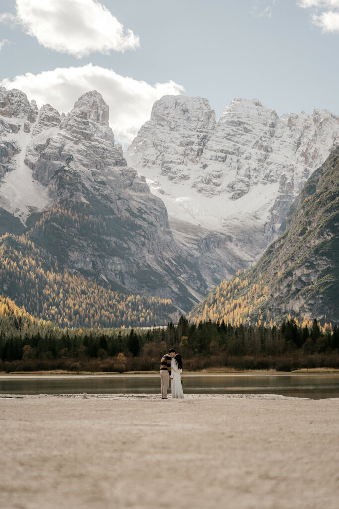 Couple stands before snowy mountain landscape.