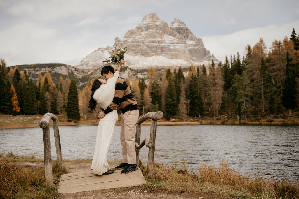 Couple kissing by lake with mountain backdrop.
