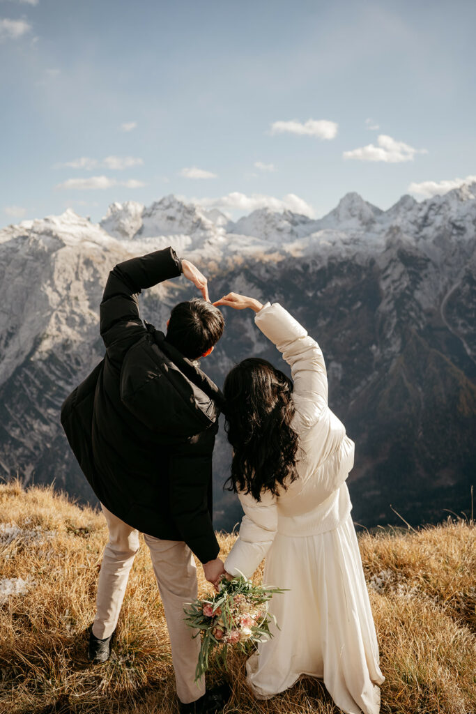 Couple making heart shape overlooking snowy mountains.