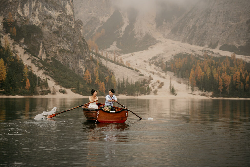 Couple rowing wooden boat on serene mountain lake.
