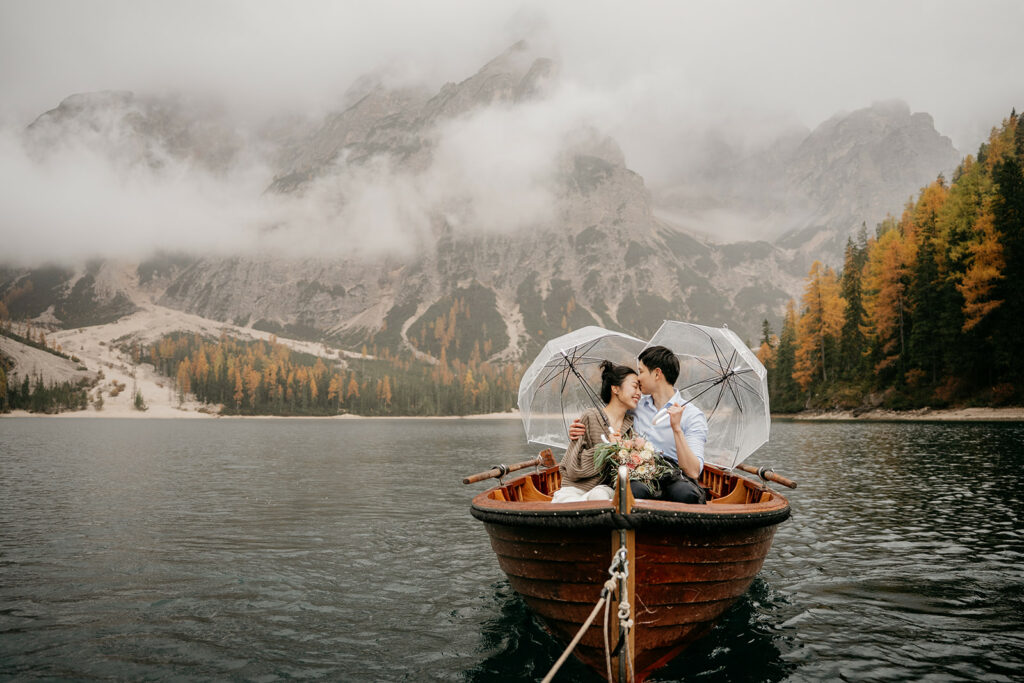 Couple in boat on misty lake with umbrellas.