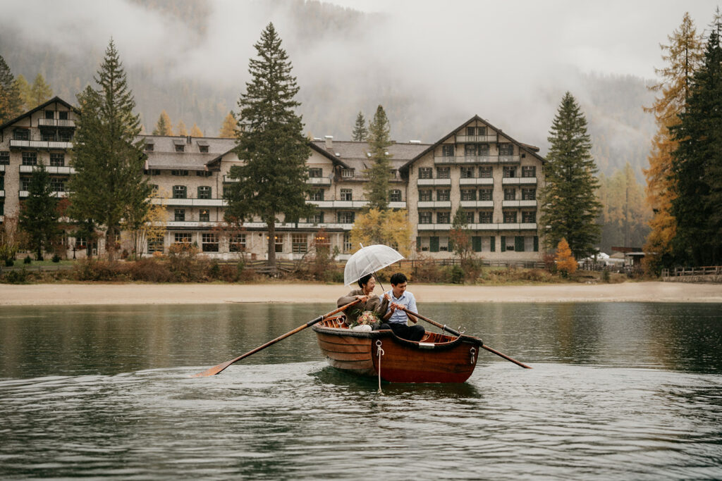 Couple rowing boat on lake near hotel.