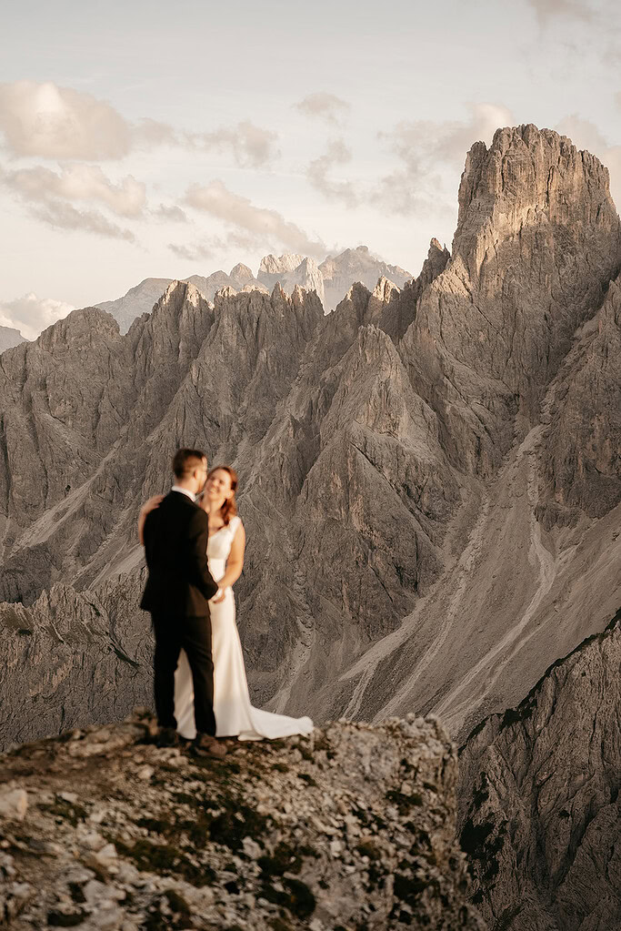 Couple stands on mountain cliff at sunset.