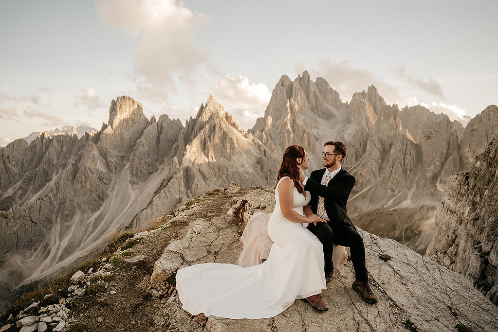 Couple in wedding attire on mountain cliff sunset.