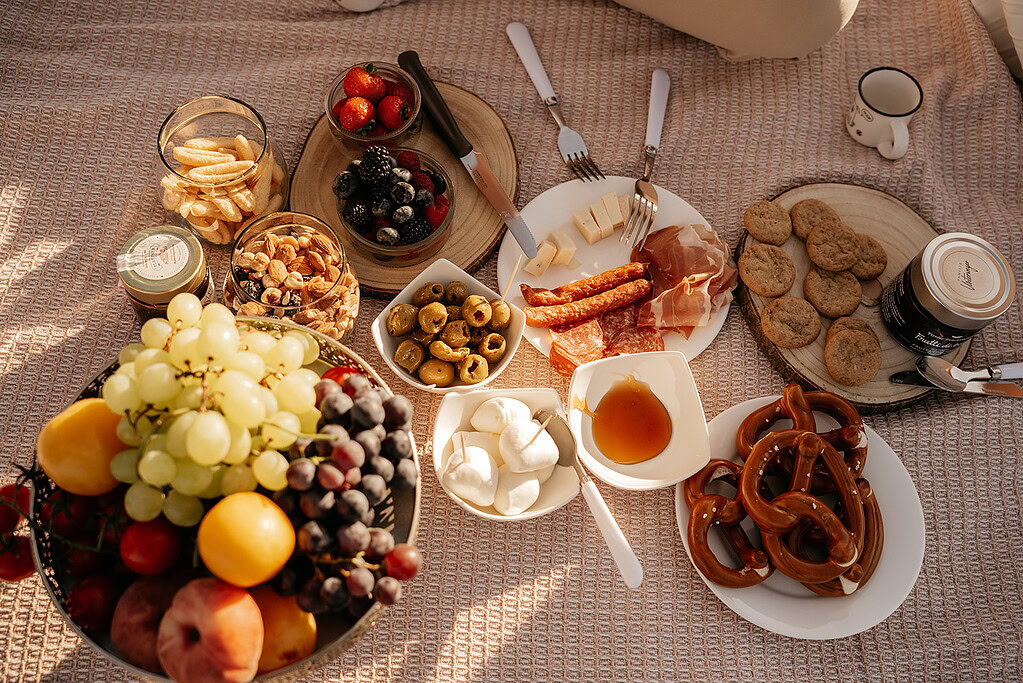 Picnic spread with fruits, cheese, and snacks outdoors.