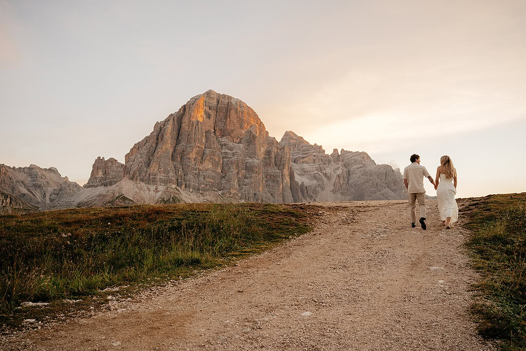 Couple holding hands walking towards mountain sunset.