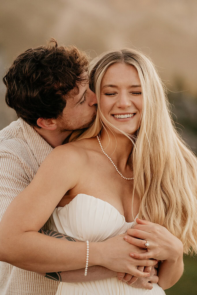 Couple embracing outdoors, woman smiling with eyes closed.
