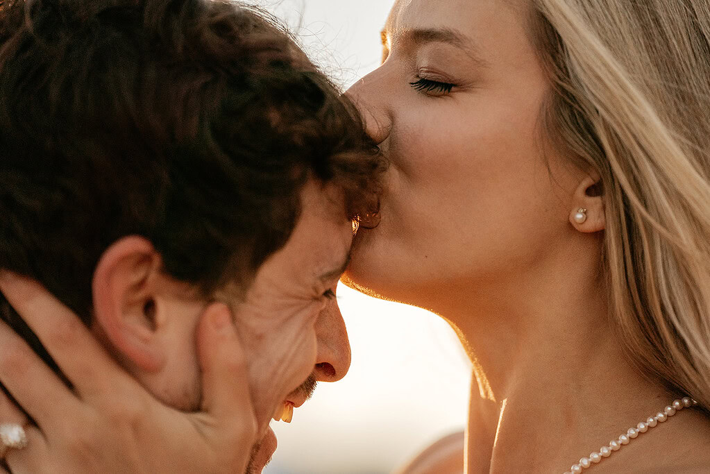 Woman kisses man on forehead, close up.